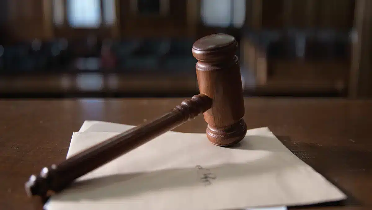 A federal judge's gavel resting on an empty desk in dim courtroom lighting, with a single threatening letter partially visible, conveying vulnerability and intimidation | judicial gavel threatening mail