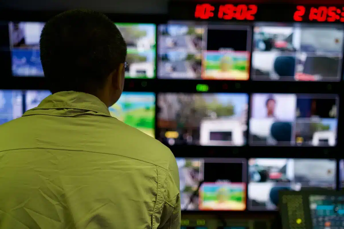 A grid control center with illuminated maps and monitoring screens, operators at workstations tracking real-time power flow across interconnected regions, cool blue and amber lighting