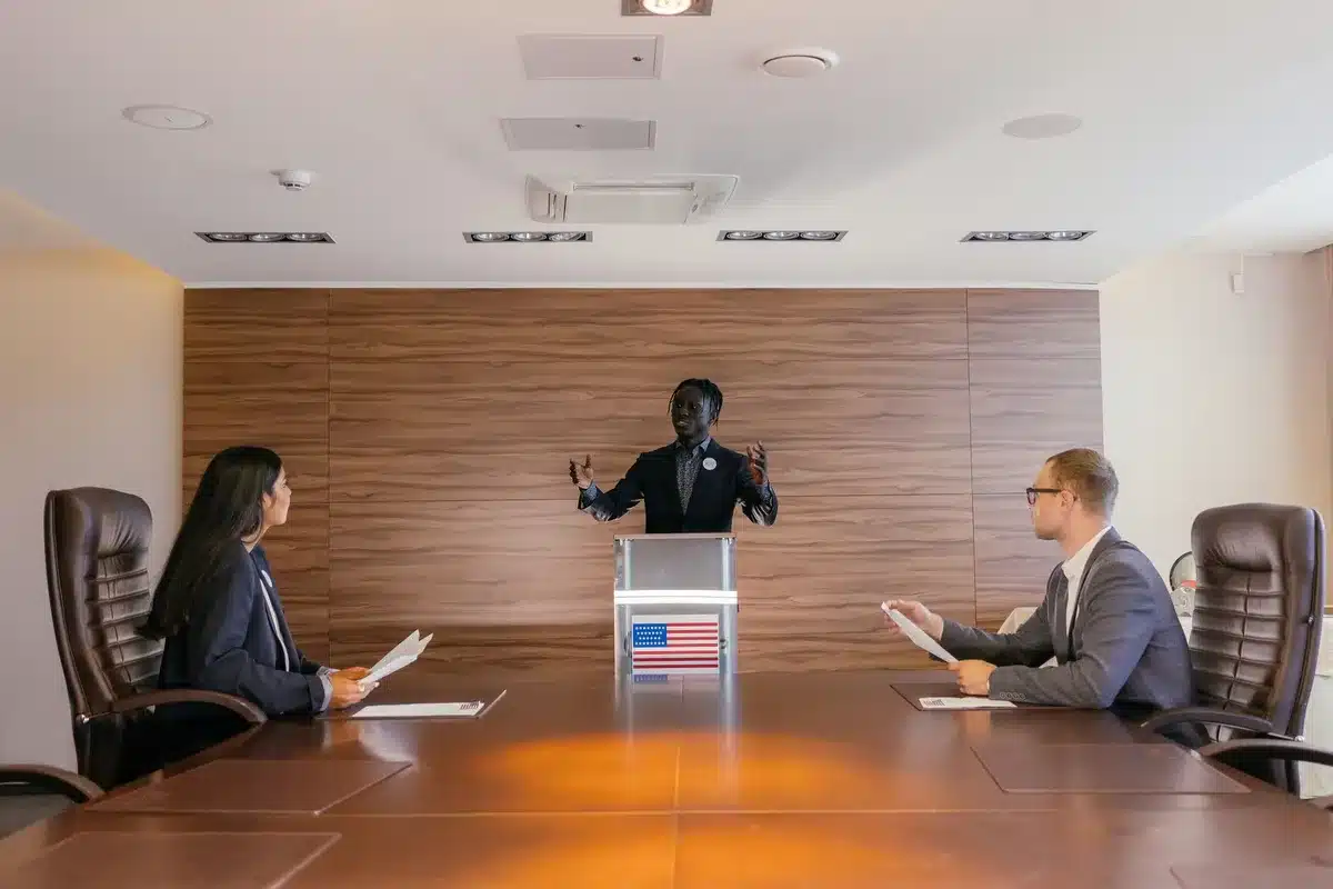 A polished wooden conference table with two nameplate holders—one reading "D" and one reading "R"—sitting side by side, papers and pens scattered between them, an open door visible in the background, suggesting ongoing dialogue and shared purpose