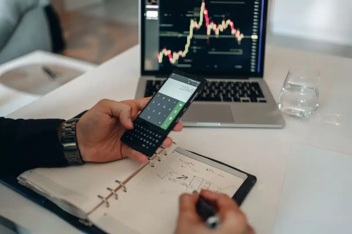 A person's hand holding a smartphone displaying stock market charts and investment portfolio data, with financial graphs glowing on the screen in soft blue light, symbolizing digital wealth management and investment growth.