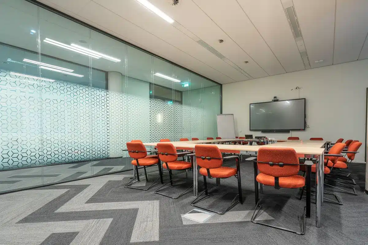 An economics conference room with a long table, papers and charts spread across it, a single empty chair at the head, soft overhead lighting casting shadows on policy documents, tension in the composition