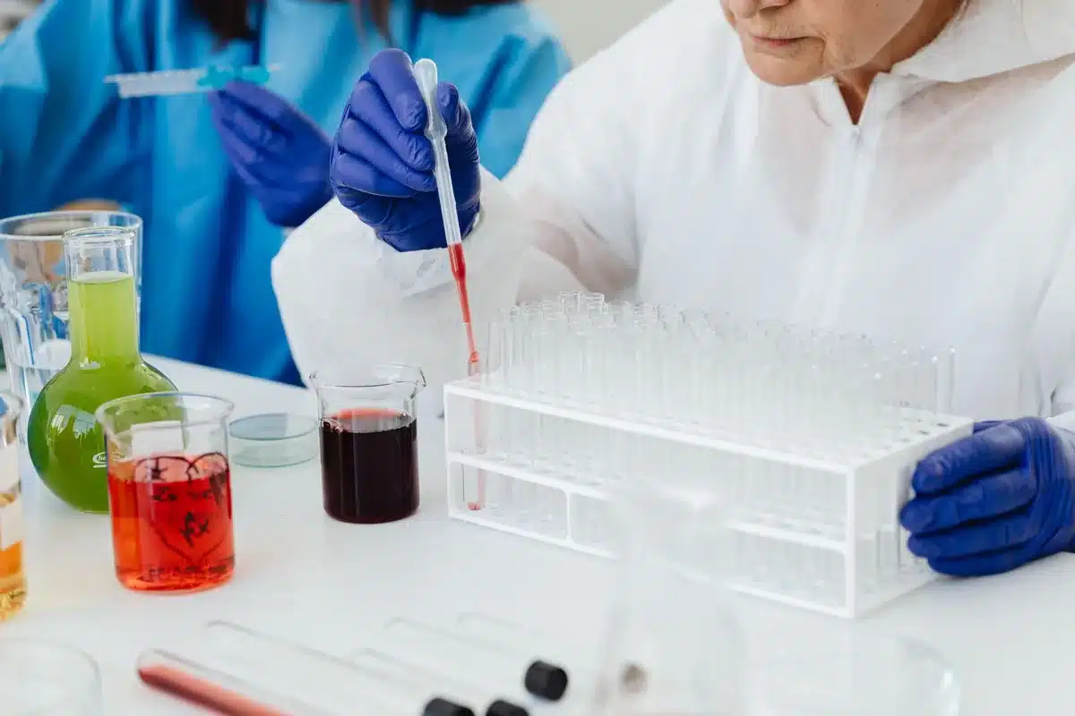 A laboratory technician in protective gear examining petri dishes with bacterial cultures under a microscope, rows of sample containers
