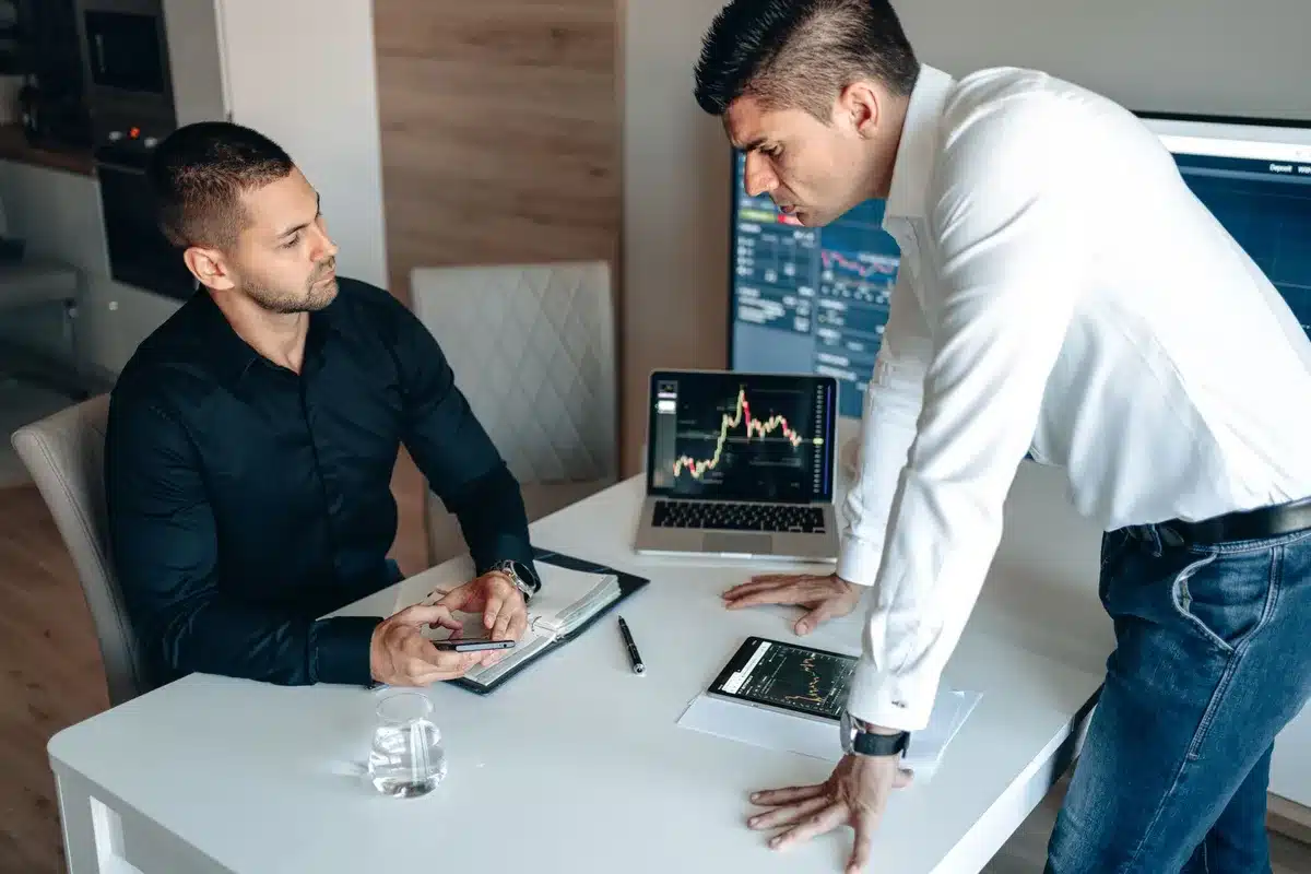 Traders collaborating in a forum discussion, multiple screens showing market data, economic calendars, and real-time price updates
