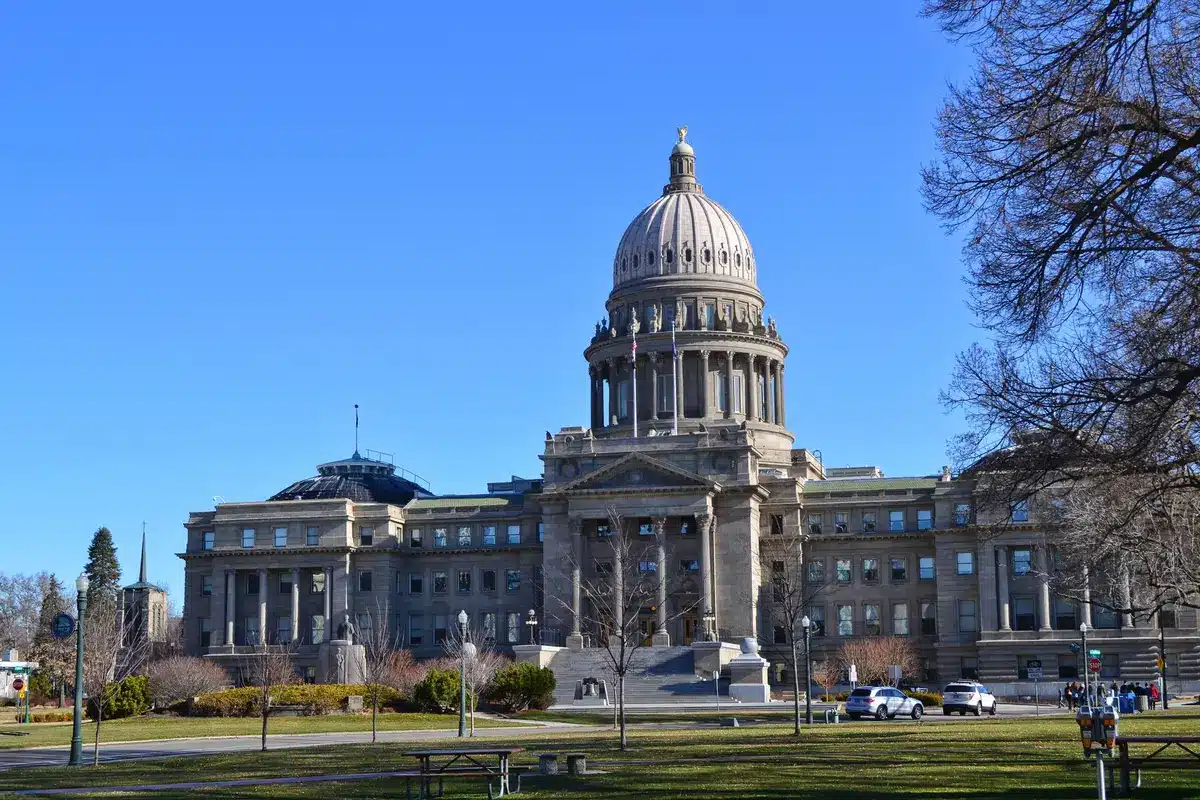 A state capitol building interior with empty legislative chambers, soft daylight through tall windows, wooden desks and voting boards visible, a sense of anticipation and democratic process suspended in time