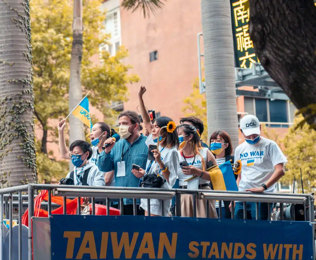 Campaign rally crowd holding "Francesca Hong for Governor" signs, diverse supporters with raised arms and enthusiastic expressions under bright outdoor lighting, grassroots energy and collective momentum