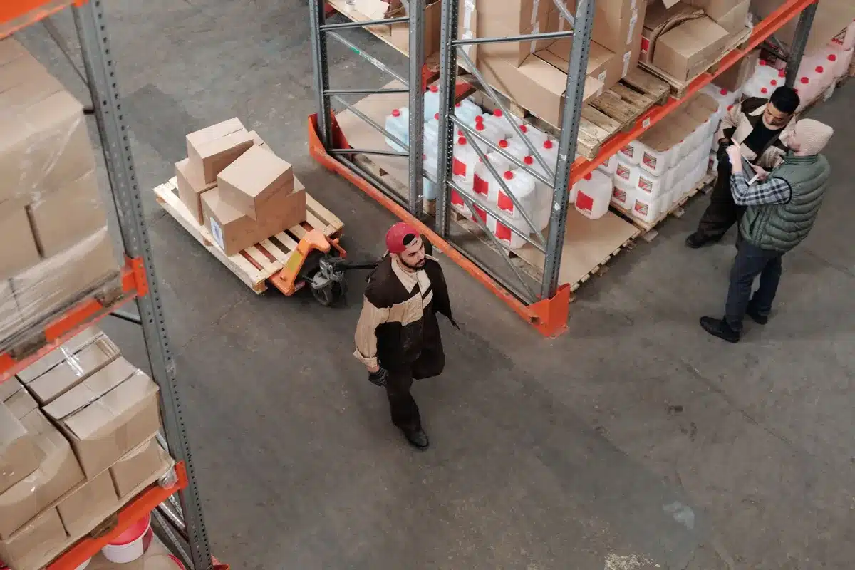 Cardboard boxes of raw beef stacked in a warehouse, labeled with foreign establishment numbers, under bright overhead lighting with shadows emphasizing the industrial storage environment