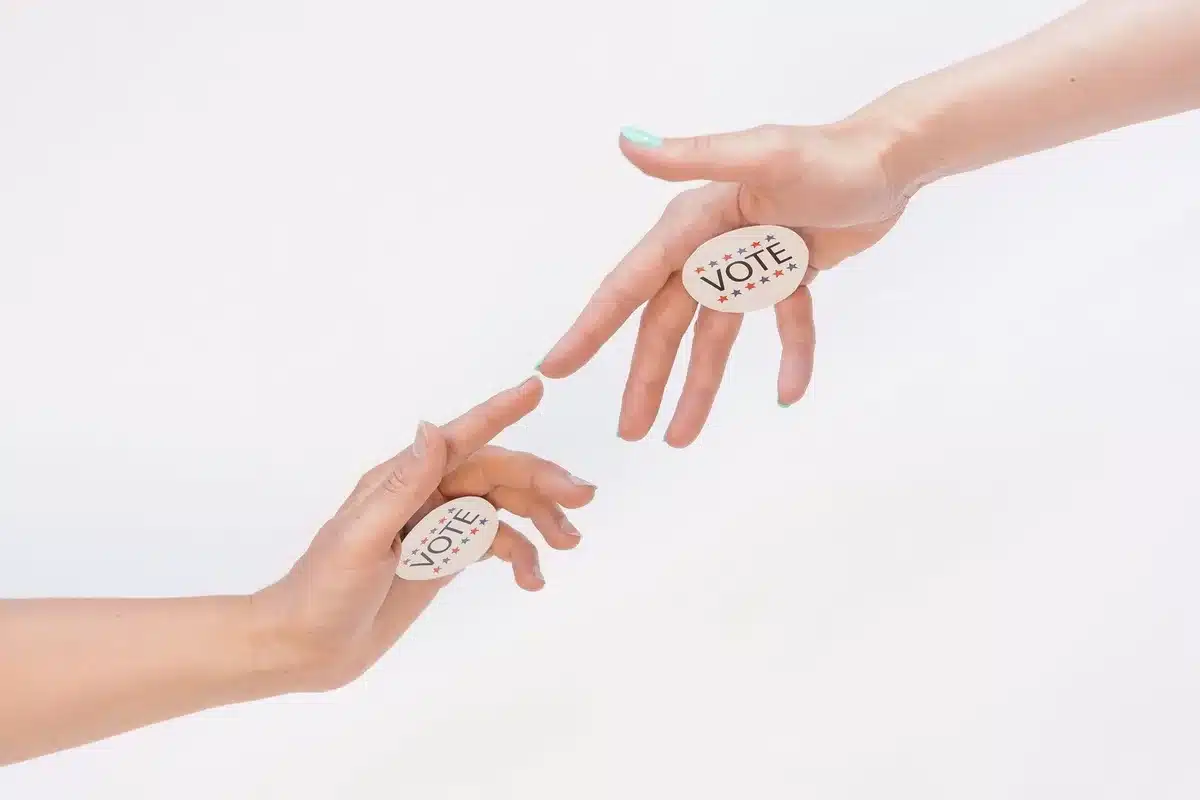 A split-screen showing a Democratic campaign button and a Republican campaign button side by side, both resting on a wooden table
