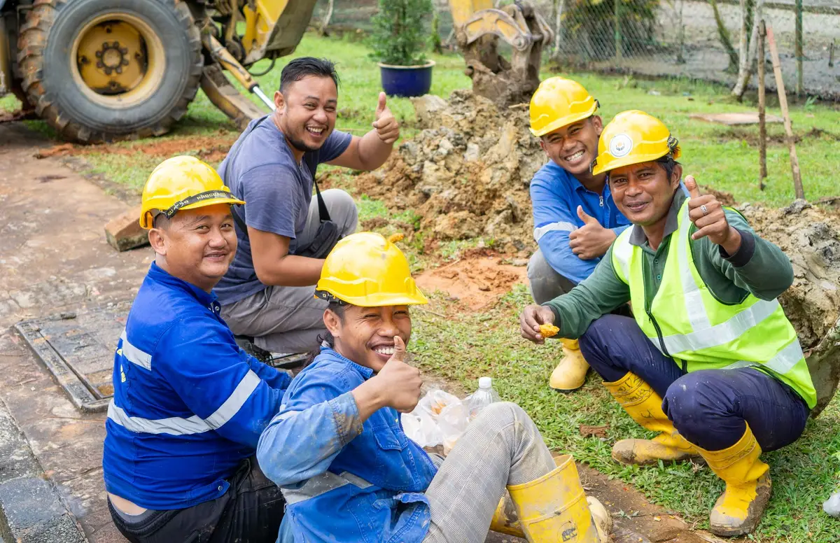 Construction workers in hard hats gathered around an open cellar wall, golden bars and coins visible in a chest, tools and dust surrounding the discovery site