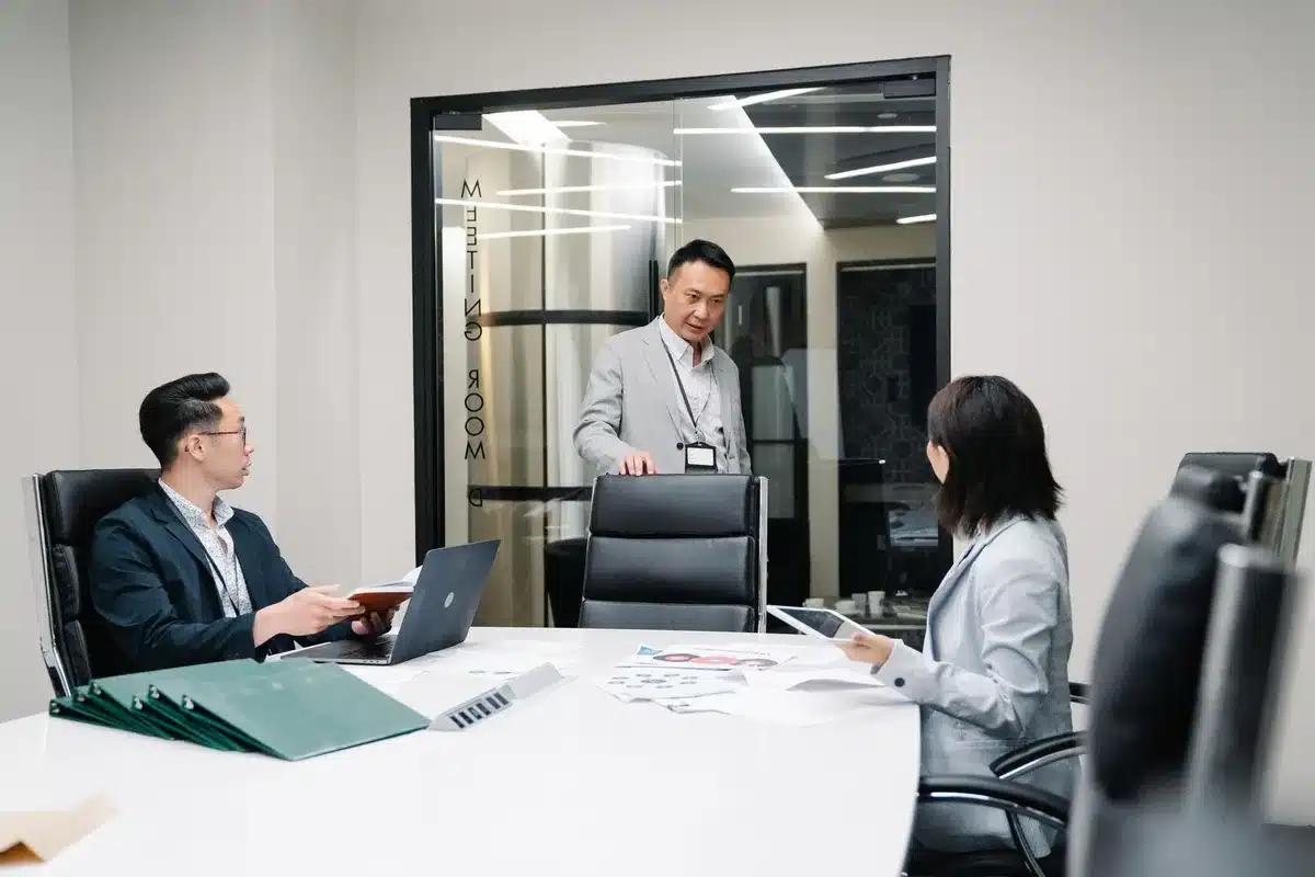 A corporate conference room with empty executive chairs arranged around a glass table, soft blue light from monitors casting shadows, a single spotlight on the head seat, tension and transition palpable