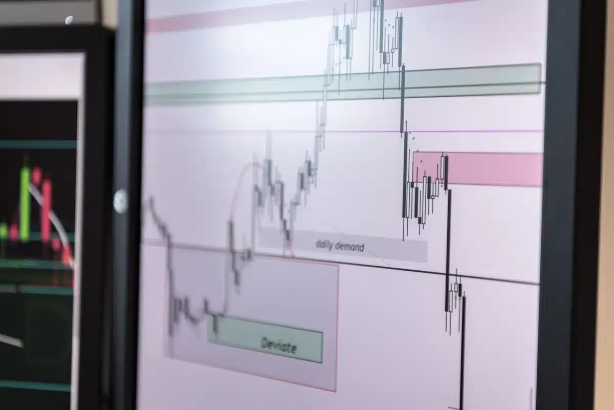 Stock market ticker display with downward trending lines in red, numbers blurring across a dark screen, financial data reflecting on glass, uncertainty and market reaction