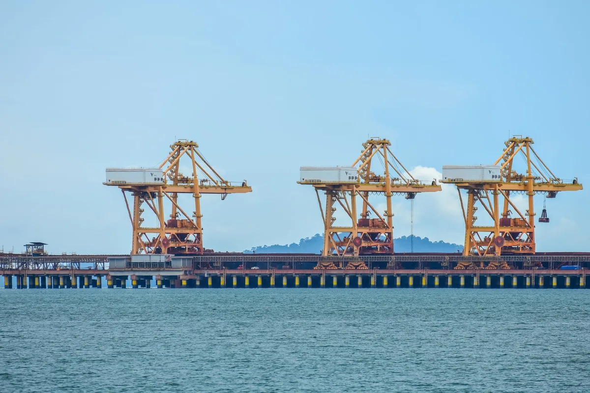 Port facility at sunset with multiple crude oil loading terminals, tanker ships at moorings, calm water reflecting industrial lights, modern infrastructure silhouetted against sky.