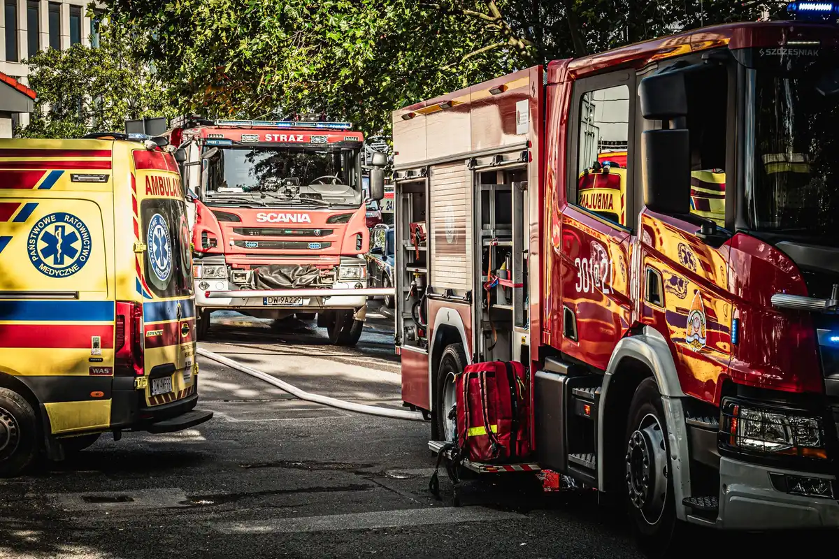 A fire truck and police car parked side by side at a station, emergency lights visible, equipment ready