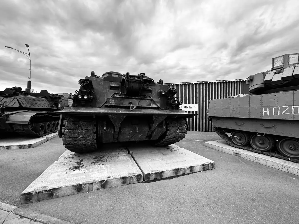 Secretary of Defense at a manufacturing facility, observing production lines of tactical military vehicles in an industrial warehouse setting