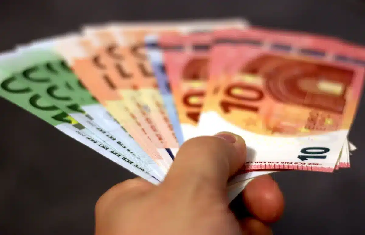 A stack of crisp dollar bills fanned out under a spotlight, casting sharp shadows on a dark surface, a single bill slightly raised, suggesting motion and value