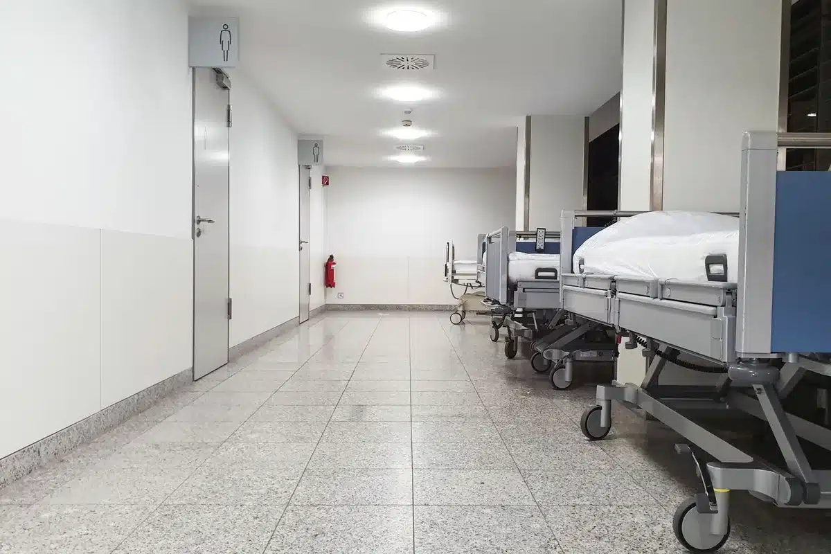 A dimly lit hospital corridor with empty chairs, soft fluorescent lighting casting long shadows on the wall, a single closed door in the distance, suggesting quiet medical spaces where difficult health news is shared