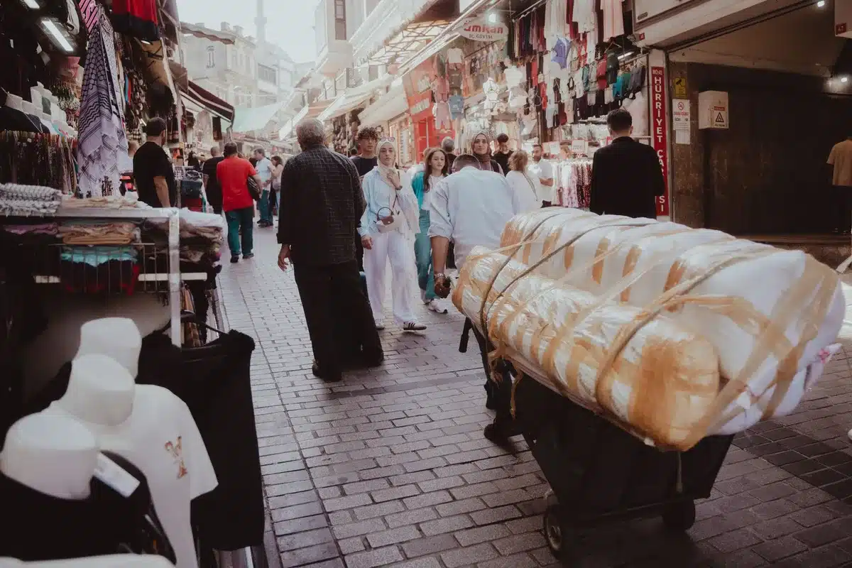 Crowded Tehran bazaar with merchants and shoppers examining goods, price tags with multiple zeros visible, anxious faces studying displays, warm afternoon light