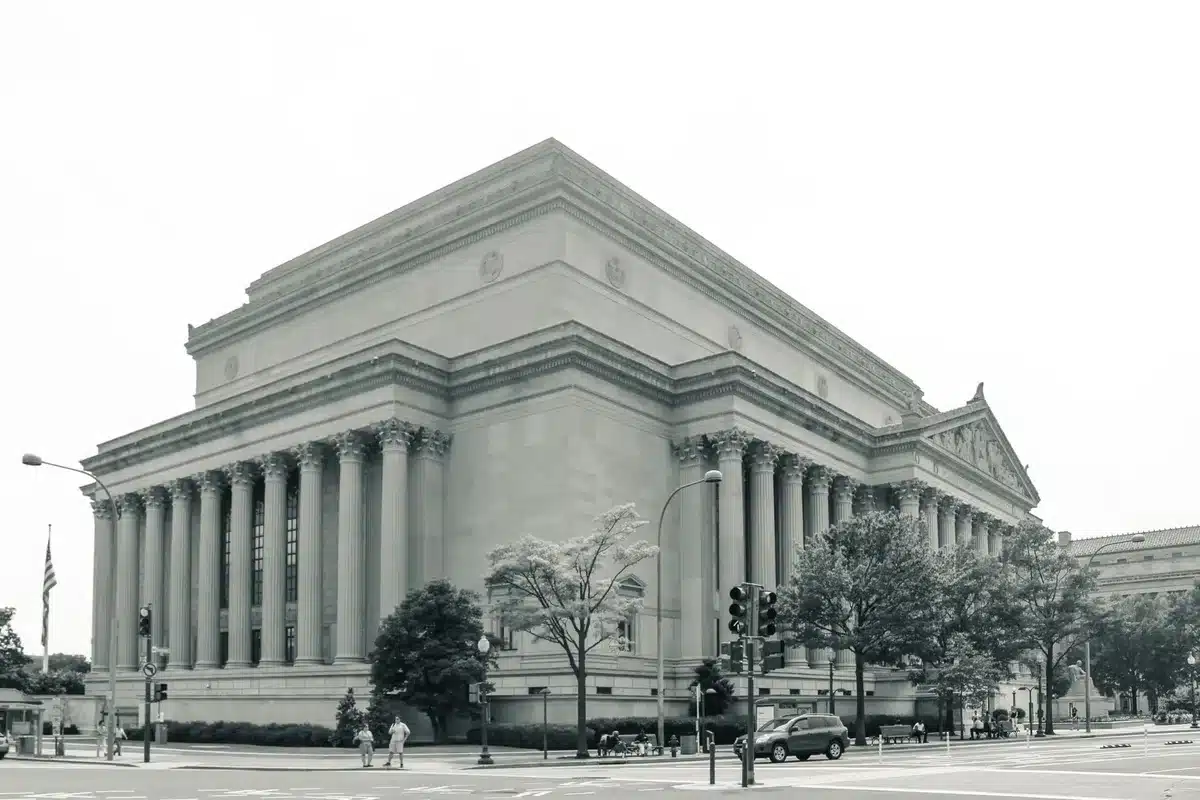 Treasury building exterior under overcast sky, harsh light on stone columns, an empty plaza stretching before it, one solitary figure walking away into shadow, sense of institutional power and isolation