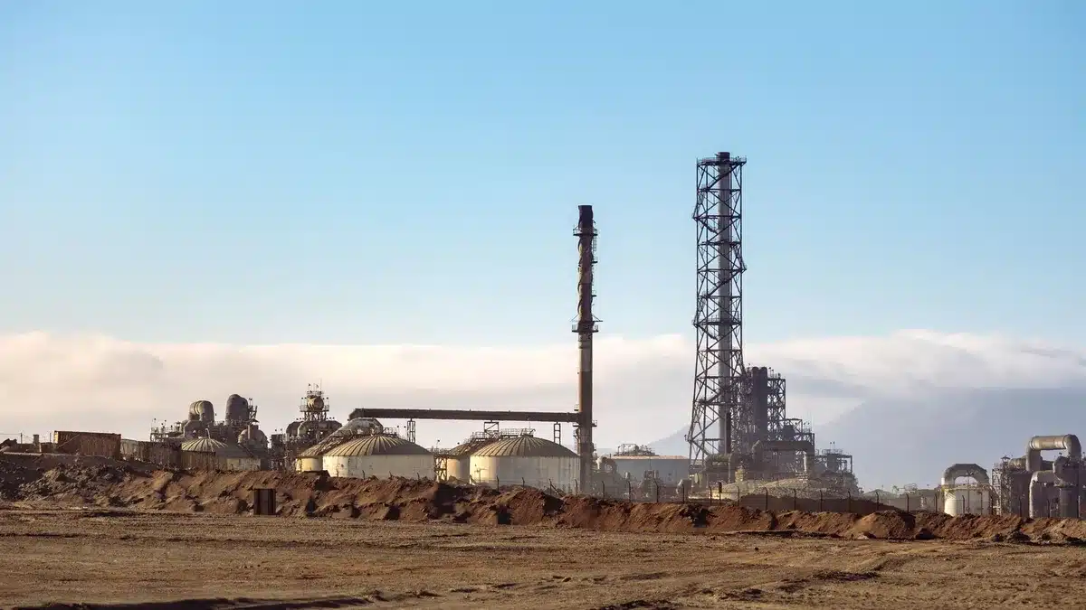 A sprawling industrial pipeline complex stretching across desert terrain, with welded sections and valve stations visible, construction equipment in the background, under clear sky