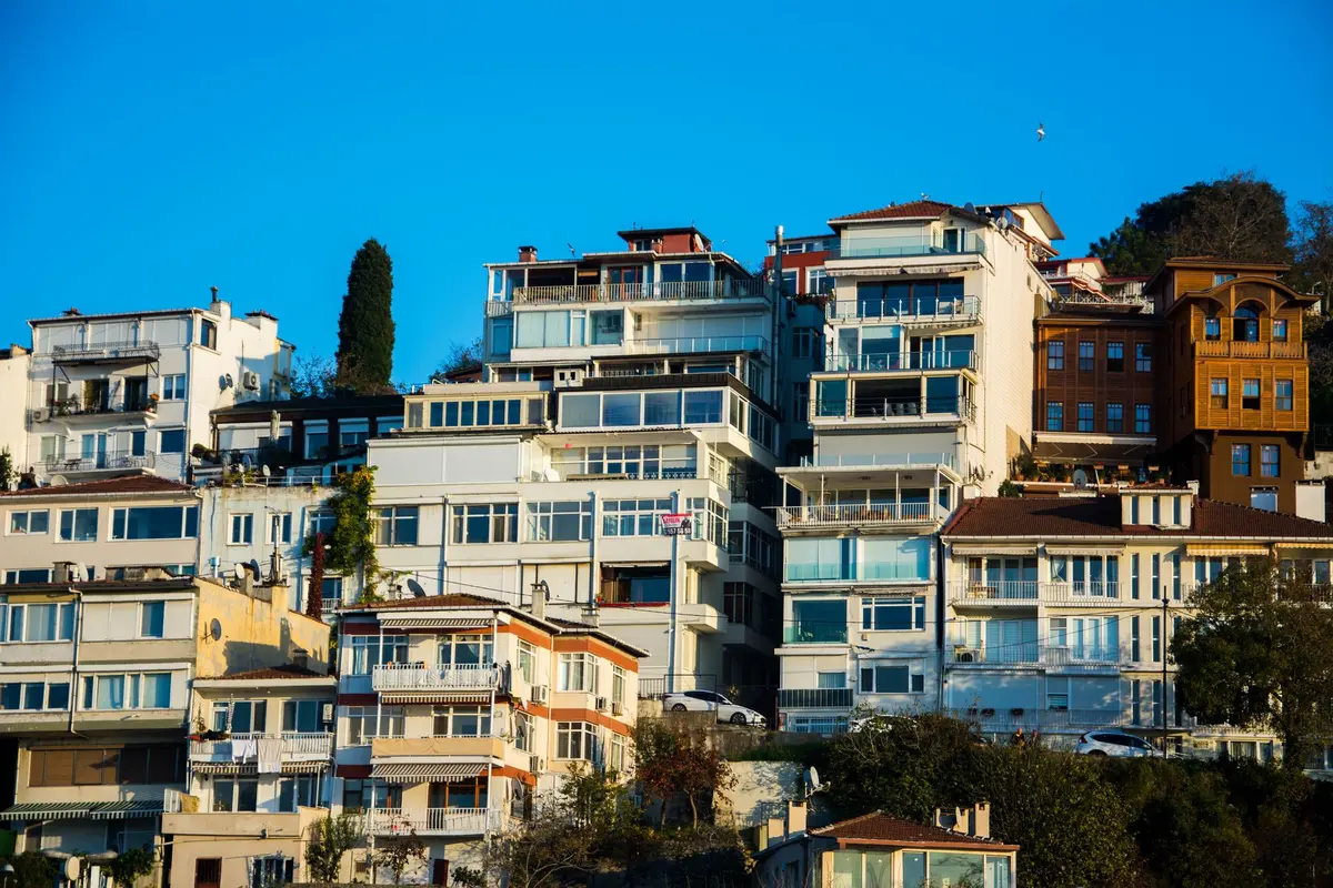 A modern residential tower at dusk with warm lighting in windows, mixed-income units visible, urban waterfront setting, reflecting a commitment to accessible housing in expensive city markets, sense of opportunity and stability