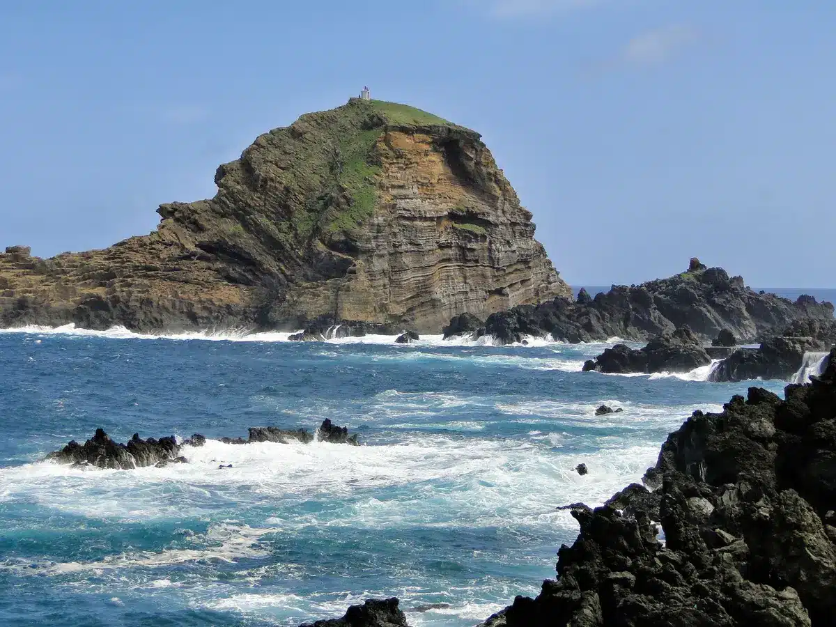 A wide view of a rocky volcanic coastline with crashing waves, steep cliffs rising from the ocean, no people visible, representing the Izu Islands' volcanic geology and seismic setting.