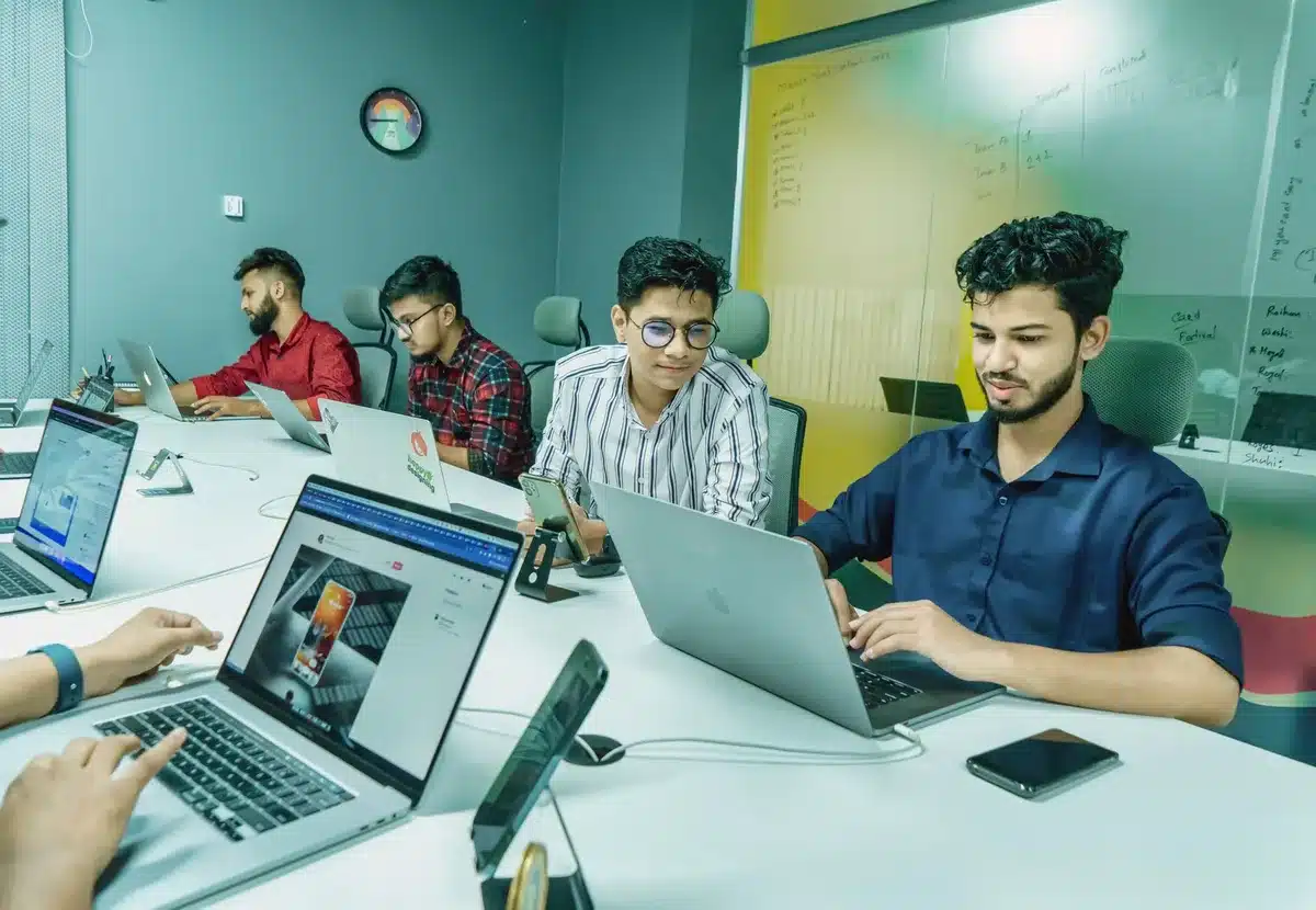 A modern startup office space with collaborative workstations, whiteboards covered in AI architecture sketches, and glowing computer screens displaying neural network visualizations in soft blue and purple light