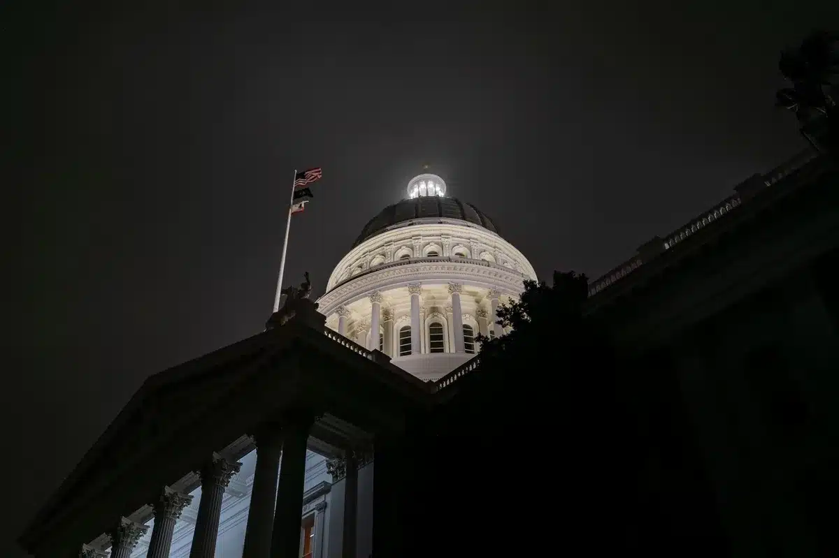 Modern state capitol building exterior at dusk, Michigan flag flying, empty legislative chamber visible through lit windows, symbolic of the executive power being contested