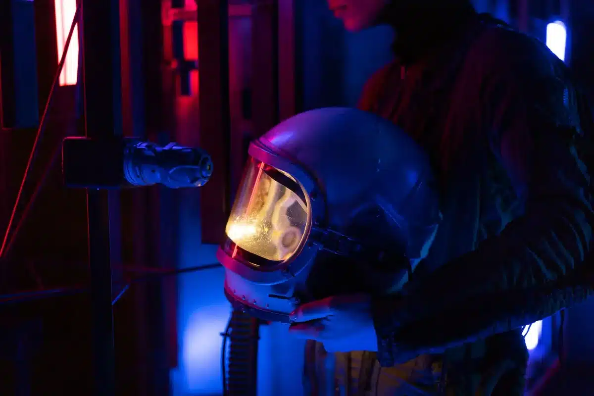 Military astronaut in flight suit standing before a spacecraft or ISS module, hands clasped, Earth visible through a window behind, reflecting service and exploration
