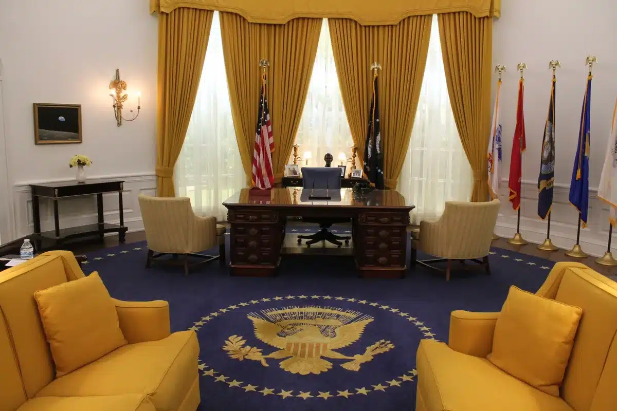 A professional woman at a podium in an official setting, speaking with focused intensity, the room blurred behind her.