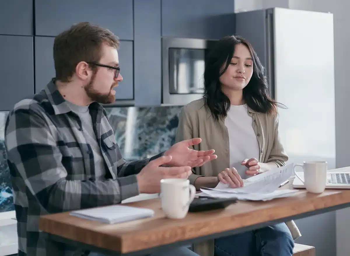 A couple sitting at a table reviewing financial documents together, with a calculator and pen nearby, discussing wedding costs and budget planning