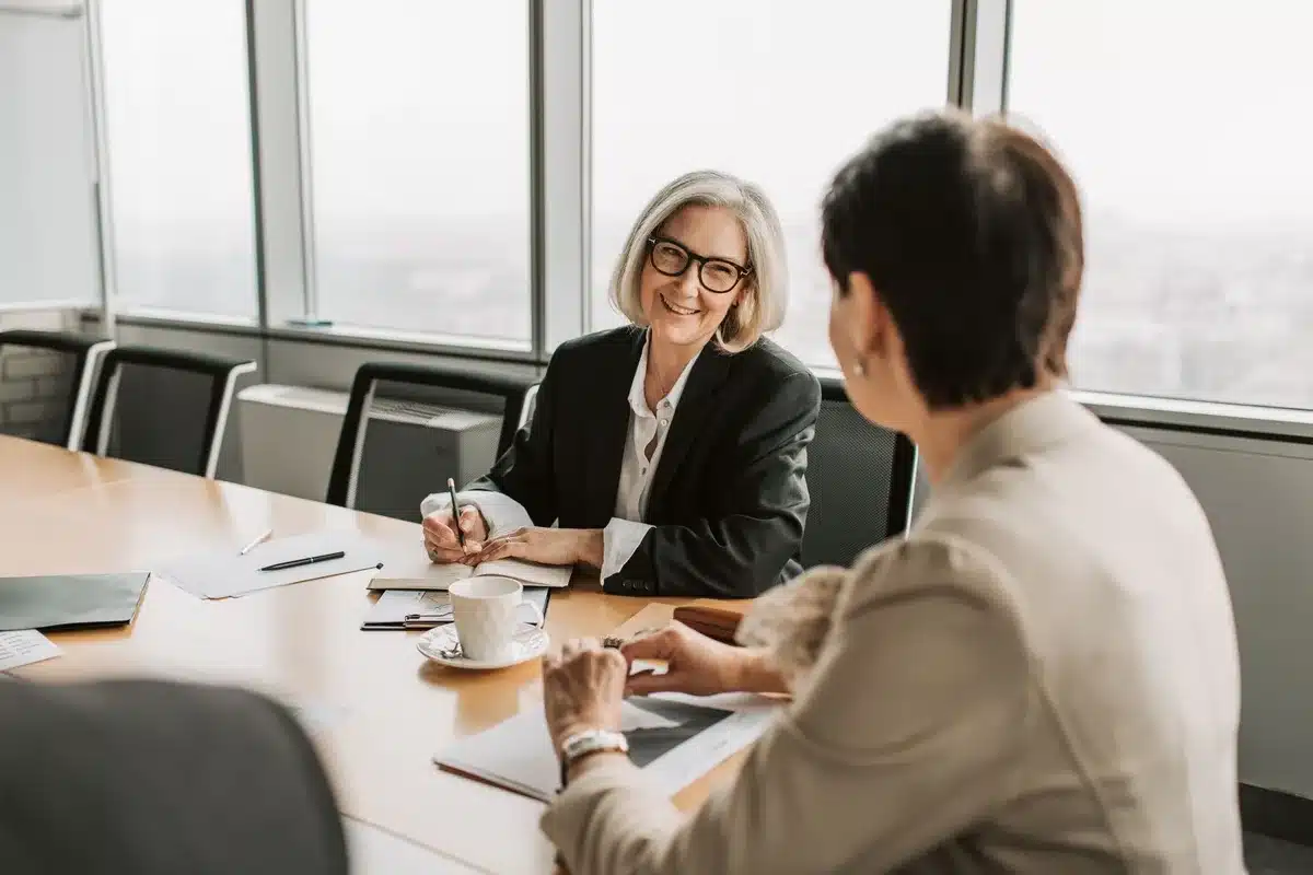 A diverse group of professional women in business attire standing together in a modern Capitol office building, smiling and confident, representing generational change and political advancement.