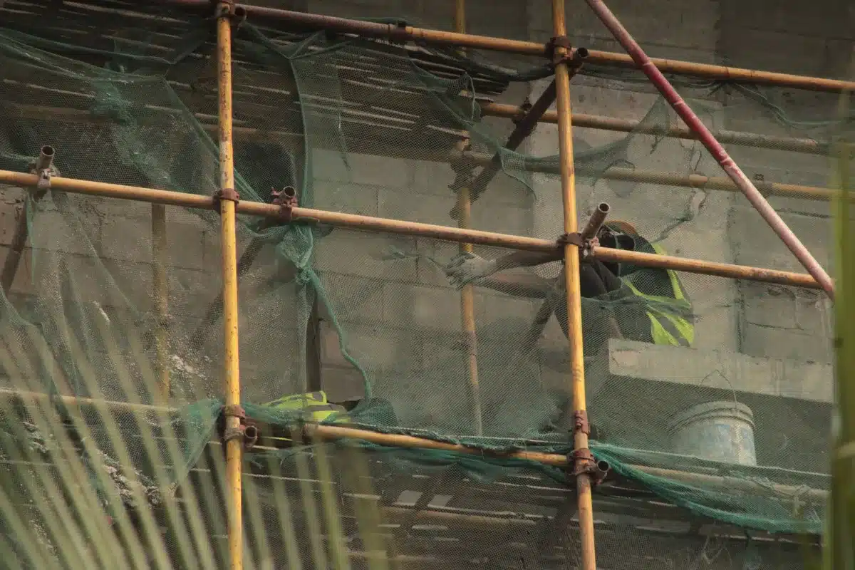 A white tarp covering the facade of a performing arts building, with metal scaffolding visible, marble panels beneath, and construction equipment on the ground.