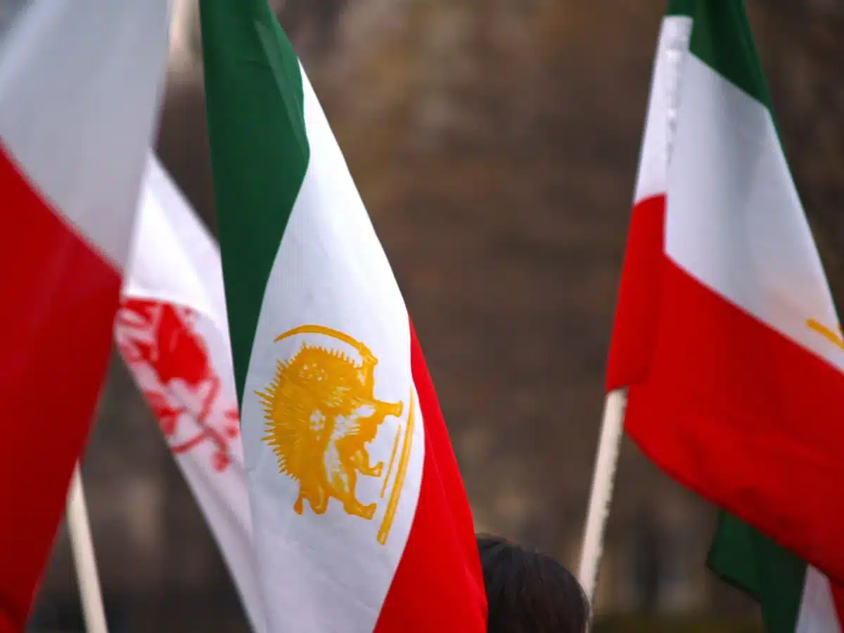 A split-screen view showing a flag of Iran on one side and the skyline of a Gulf city on the other, separated by a jagged line, symbolizing the divide between Iran and Gulf states.