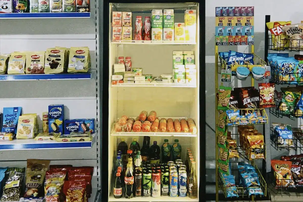 Shelves of chocolate chip bags in a warehouse bulk store, packages stacked high with product labels visible, customers browsing the baking aisle