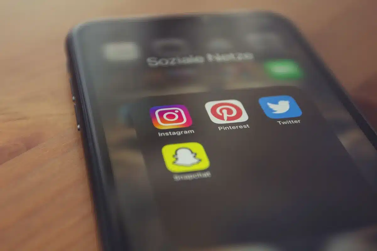 A smartphone screen glowing in darkness, displaying harsh social media text, the device held in shadow suggesting digital confrontation and targeting