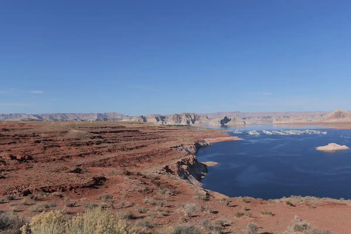 Exposed rocky shoreline with white mineral deposits marking former water line, abandoned dock pilings, bathtub ring visible on canyon walls, desert landscape stretching to horizon