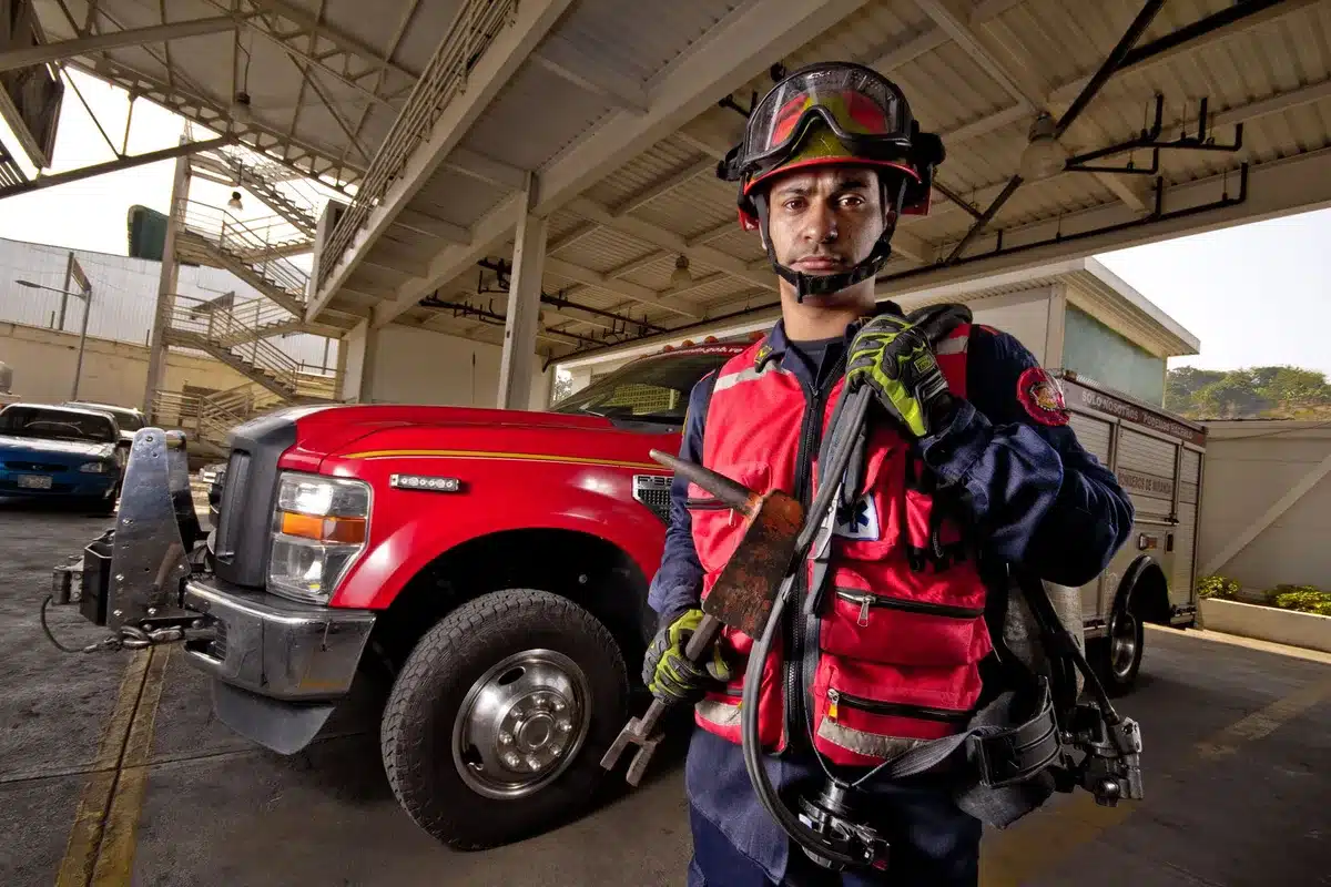 A fifth-generation firefighter in dress uniform standing in a professional setting, with fire department insignia visible in the background, conveying leadership and regional fire service expertise.
