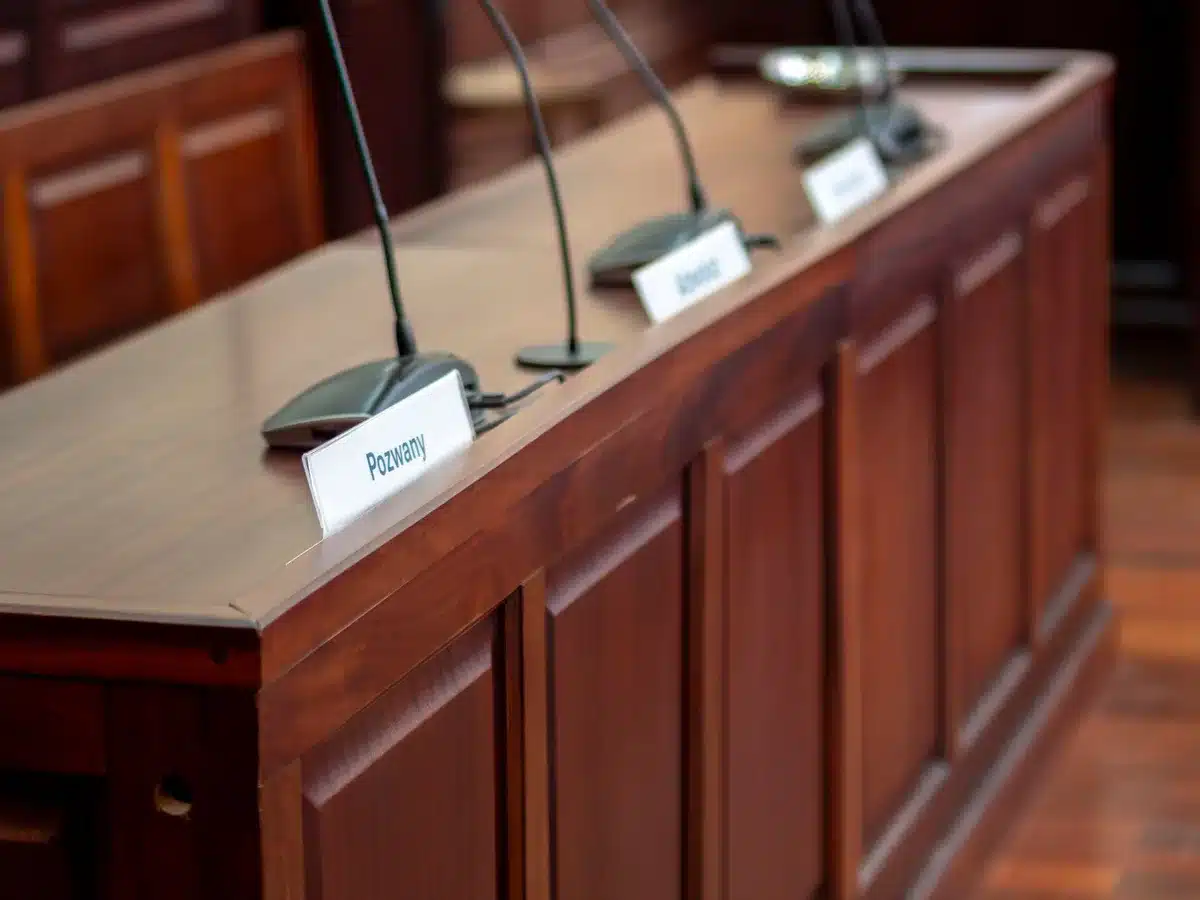 A courtroom interior with empty defendant chairs, harsh fluorescent lighting, and a judge's bench in shadow, symbolizing the dropped legal case.