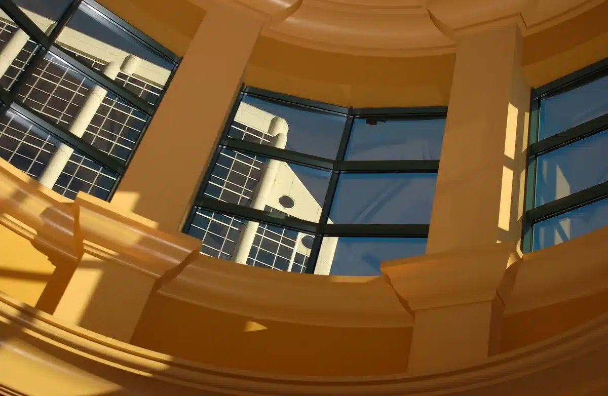 Dimly lit federal courthouse entrance with marble columns, a single gavel resting on an empty judge's bench, morning light streaming through tall windows, papers scattered below, tension and legal weight evident