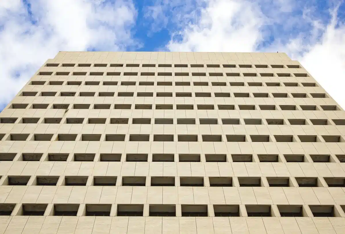Federal Reserve building exterior at dusk, American flag at half-mast, empty plaza in foreground, architectural detail of the building's classical facade, subtle light on the seal, solemnity and institutional weight