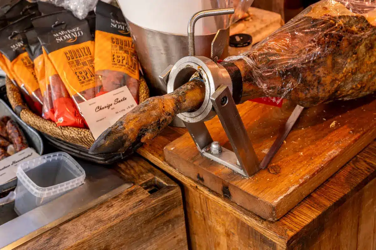A foodservice kitchen counter with stainless steel surfaces and sealed cardboard boxes of deli meat products in cool lighting, suggesting commercial food storage and safety protocols.