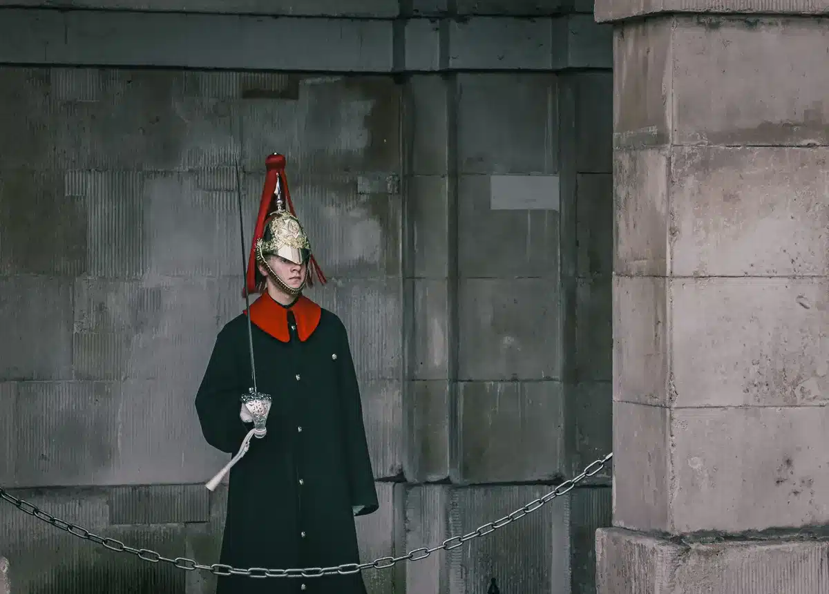 Military officer in dress uniform standing alone in a sparse government corridor, hands at sides, fluorescent light casting long shadows, expression grave and composed, tension visible in the stillness