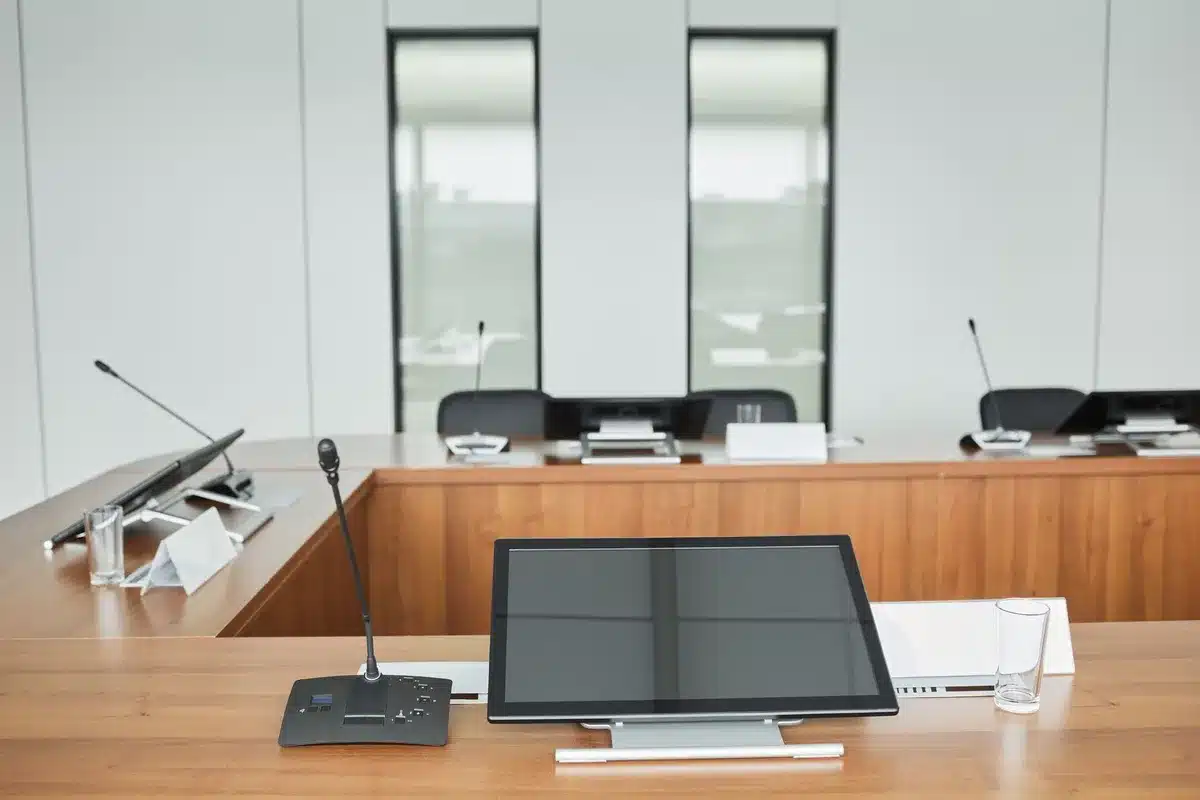 A formal government conference room with an empty mahogany table and chairs, morning light streaming through tall windows, neutral office setting with no identifying plaques or insignia visible, suggesting an official advisory body in session.