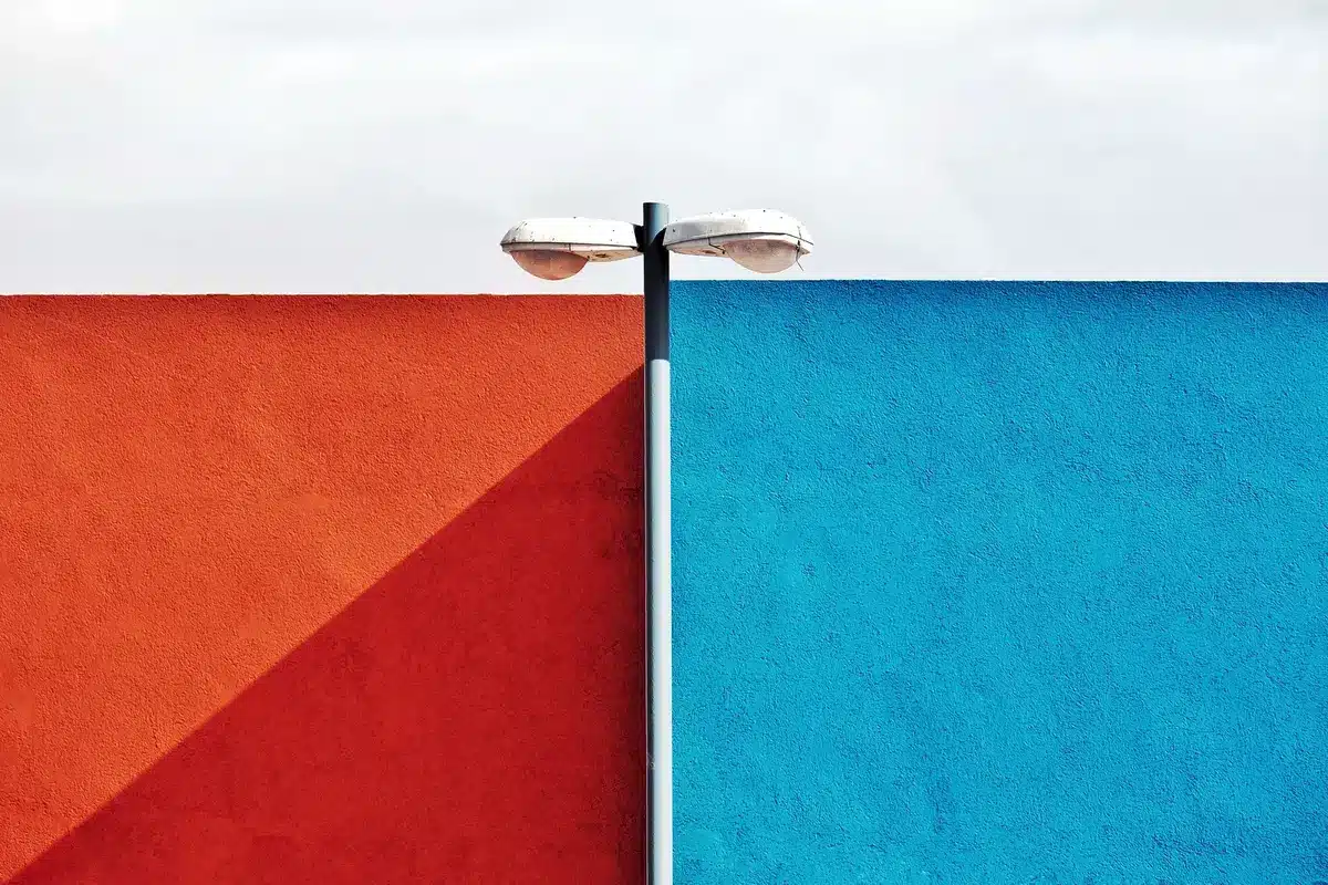 A split-screen frame showing a microphone in harsh red light on one side and an empty chair in cool blue shadow on the other, representing conflict and division.