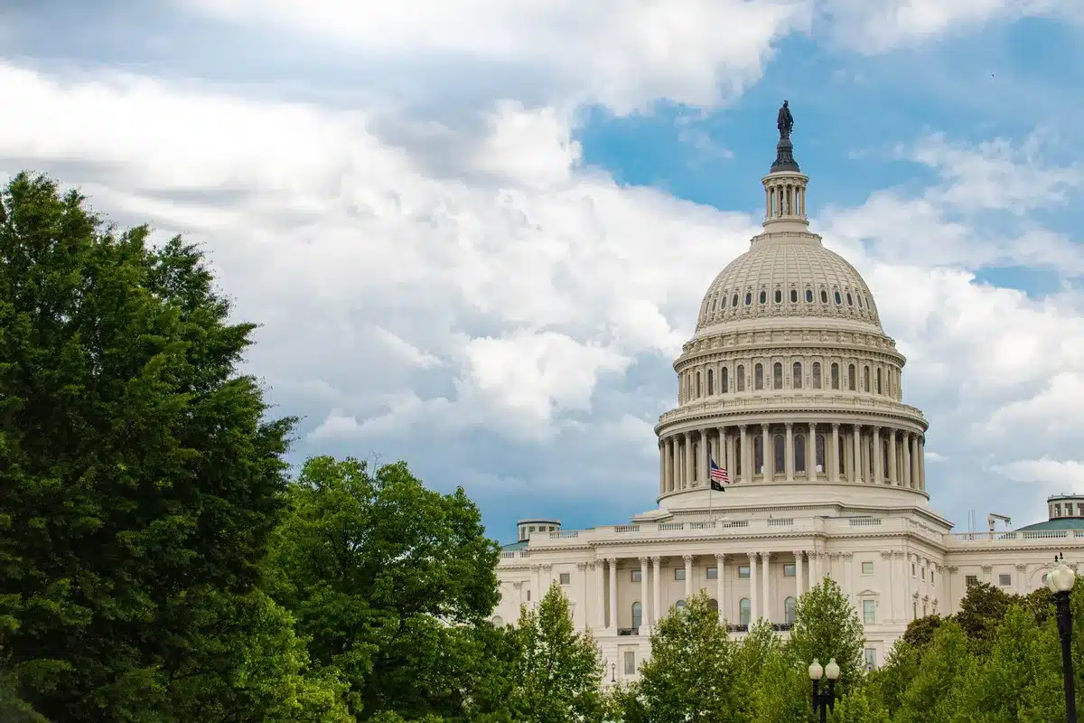 An empty congressional office with a lone desk and chair, soft light filtering through vertical blinds, papers scattered on the floor, a sense of political turmoil and uncertainty