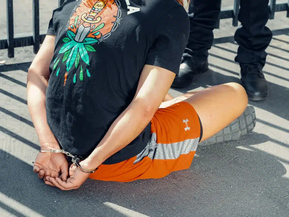 Federal agents in tactical gear restraining a figure during a chaotic scene outside a detention facility entrance, body cameras visible, the moment of physical contact captured mid-motion.