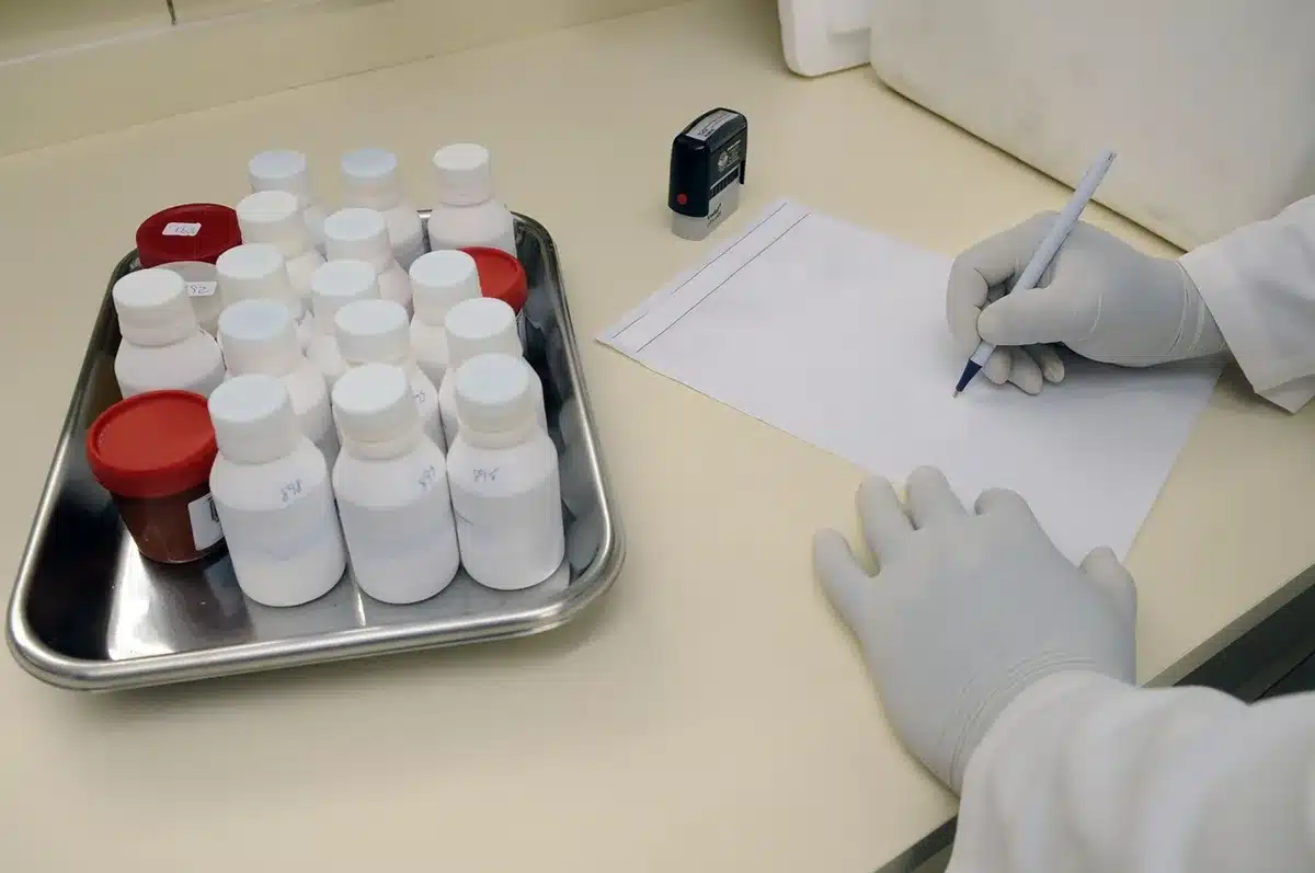 Pharmaceutical laboratory with researcher examining data on a glowing monitor, vials and equipment on a clean white bench, focused intensity in a modern biotech facility