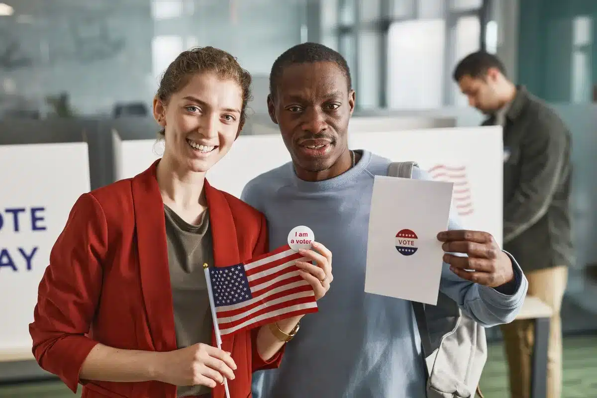 A diverse crowd of Democratic voters walking out of a polling place, some holding "I Voted" stickers, with campaign signs visible in the background