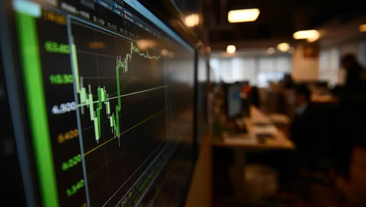 A glowing stock ticker displaying climbing numbers and green candlestick charts on a dark screen, with soft focus office lights in the background | stock market screen