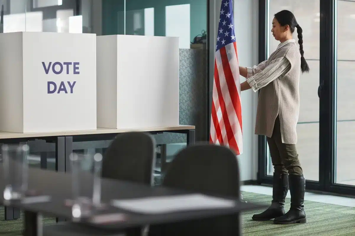 A crowded polling location with voters standing in a line, some holding completed ballots, diverse faces showing focus and engagement, sunlight through windows, the energy of civic participation.
