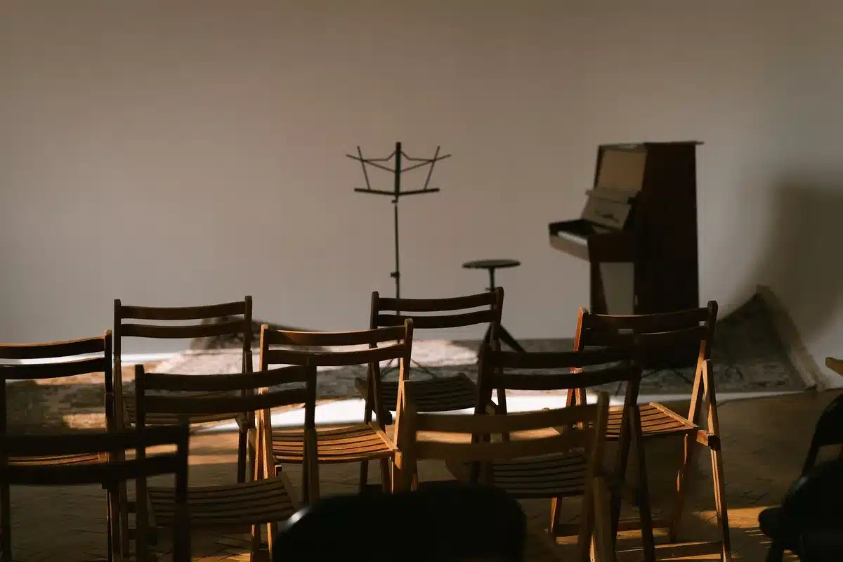 A split-screen composition showing two empty chairs facing each other across a debate stage, one bathed in warm light and one in cool shadow, a center line dividing the frame, the contrast suggesting opposing forces and political tension